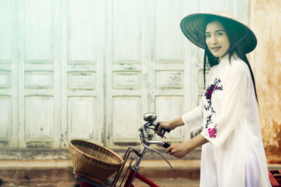 Portrait of woman holding bicycle while standing against building