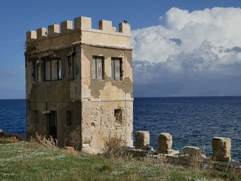 Old building by sea against sky