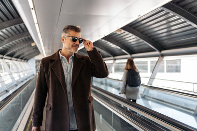 Man holding sunglasses while standing on escalator