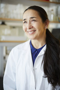 Smiling mature female teacher looking away while standing in university classroom