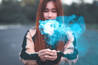 Portrait of young woman holding camera while standing outdoors