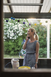 Happy woman using mobile phone while standing in log cabin during party