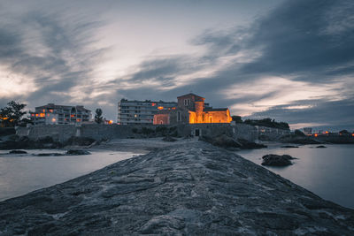 Buildings by sea against sky at sunset