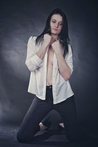 Seductive woman wearing formals kneeling against gray background