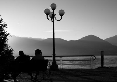 Rear view of people sitting on lake against sky