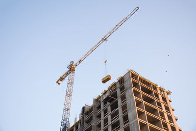 Low angle view of crane by building against clear sky