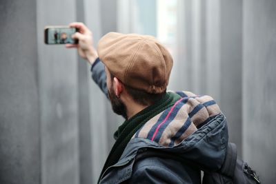 Side view of man taking selfie against wall