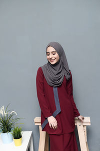 Portrait of smiling young woman standing against wall