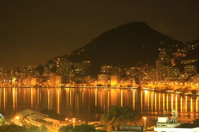 Illuminated cityscape by mountains against sky at night