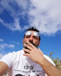 Low angle view of mature man wearing sunglasses while smoking cigarette against sky