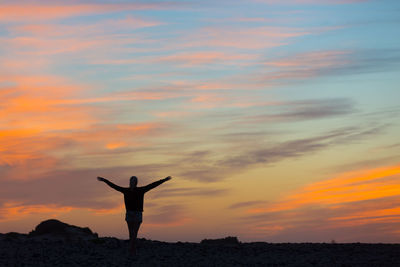 Silhouette man standing on rock against sky during sunset