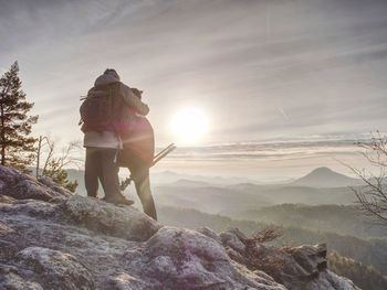 Man photographer and woman traveler photographing with the camera on the tripod. two people hugging