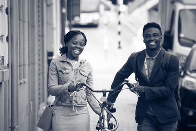 Smiling friends with bicycle walking on footpath in city