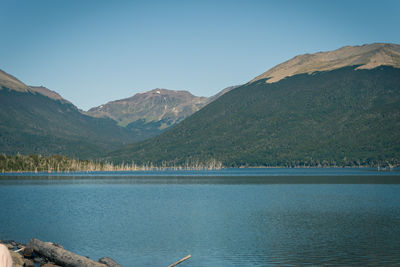 Scenic view of lake by mountains against clear blue sky