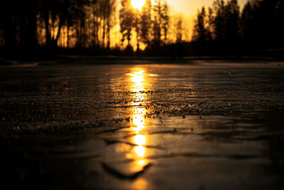 Surface level of wet road against sunset sky