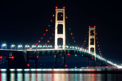 Illuminated mackinac bridge over lake against sky in city