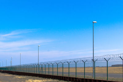 Street light and barbed wire fence against blue sky