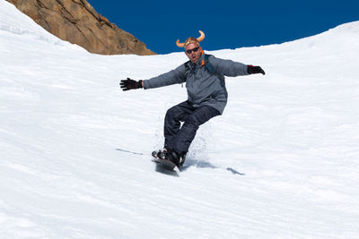 Snowboarder running down the slope in ski resort with a funny hat.