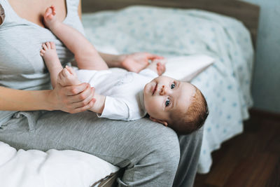 Young mother having fun with cute baby girl on her knees sitting on bed at home, love emotion