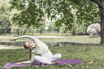 A young beautiful slender girl with long blonde hair does yoga in the summer in nature  in the park.