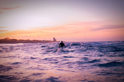 Silhouette person in sea against sky during sunset