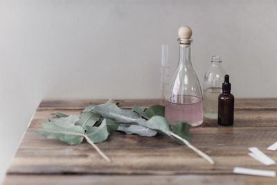 Perfume bottles with litmus strips and leaves on wooden table against wall at workshop