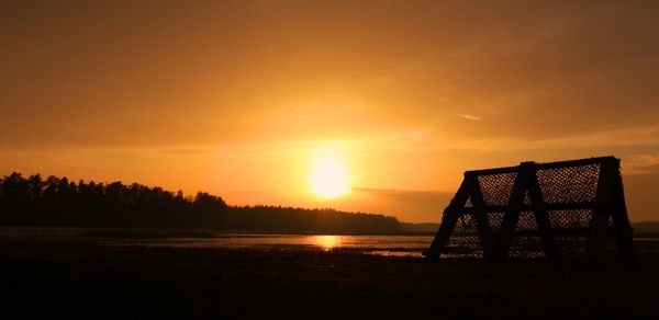 Silhouette gazebo on beach against sky during sunset