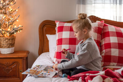 Cute girl drawing on paper while sitting on bed