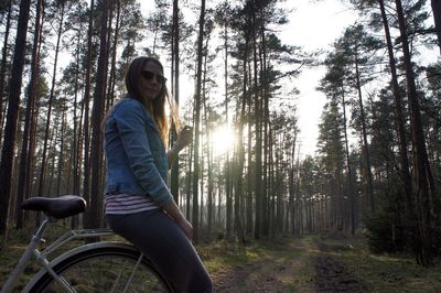 Woman sitting on bicycle against trees at forest