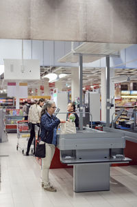 Woman with shopping bag standing by checkout counter at supermarket