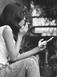 Midsection of woman holding cigarette while sitting outdoors