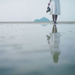 Low section of woman with reflection standing on beach