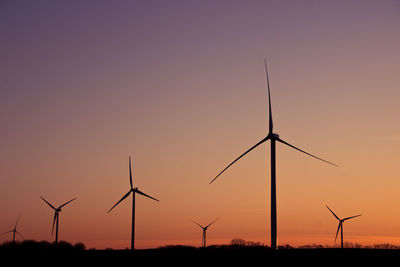 Silhouette wind turbines on field against sky during sunset