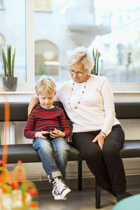 Grandmother and grandson using smart phone while sitting in waiting room of orthopedic clinic