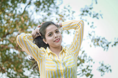 Portrait of smiling young woman against trees and sky