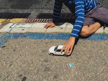 Midsection of boy playing with toy car on footpath