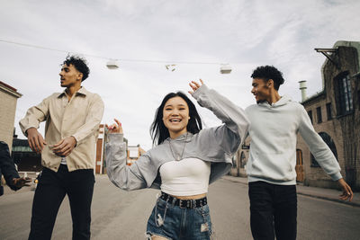 Happy multiracial young woman dancing with friends on street in city