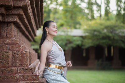 Young woman in traditional clothing looking away while sitting on building wall