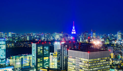 Illuminated buildings against blue sky at night