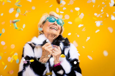 Happy senior woman standing against yellow background