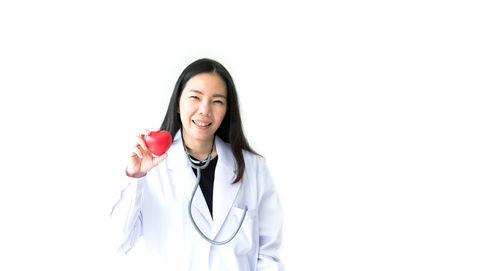 Portrait of smiling female doctor holding heart model against white background