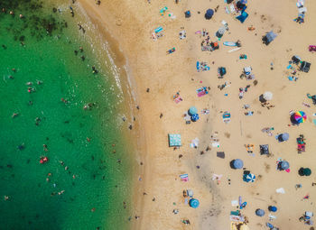 Top view drone aerial of lively sandy beach with turquoise waters during a sunny summer day.