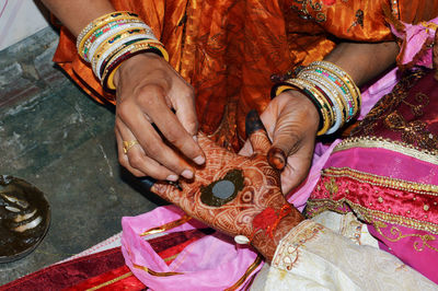 Woman put henna on groom hand to prepare for hand matching ceremony.