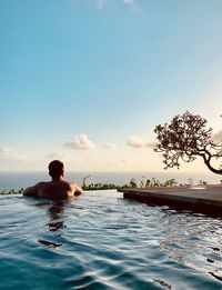 Rear view of man relaxing in swimming pool against sky