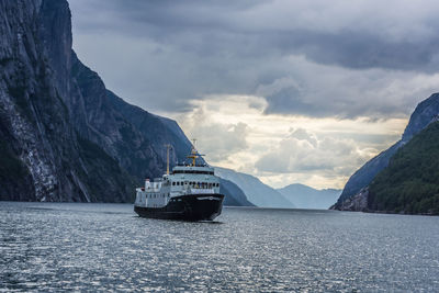 Ferry sailing on fjord by mountains against sky