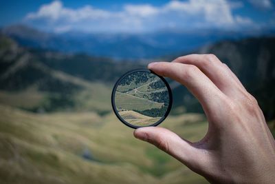 Close-up of hand holding magnifying glass against landscape