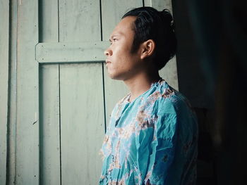 Side view of young man looking away against door