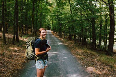 Portrait of smiling young woman standing on road in forest