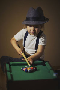 Charming child in retro clothes playing toy billiards.