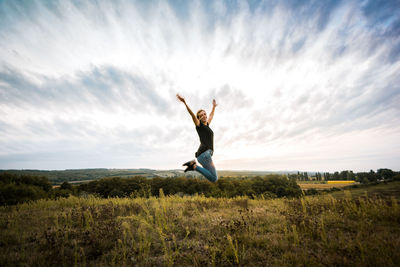 Young woman jumping with arms outstretched against sky